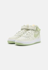 Zapatillas Nike Air Force 1 Mid en piel verde claro con suelas blancas, punta perforada, correa ajustable y acentos de logo bordado.