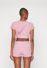 Rosa idretts crop topp med korte ermer og tonet Nike-logo på ryggen. Kombinert med matchende høyt midje shorts, glatt stoff, kroppsnær passform.