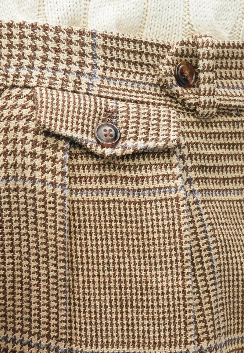 Brown and beige checkered trousers with a textured finish. Features a button detail and a front pocket flap. Accented with light blue lines.
