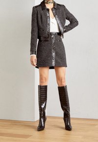 Ensemble veste et jupe en tweed noir avec accents en cuir, présentant de grands boutons et une coupe ajustée. Bottes brillantes montantes avec motif crocodile.