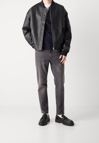 Svart läder bomberjacka med quiltad krage, i kombination med grå jeans och svarta chunky loafers, som visar upp släta texturer och modern design.