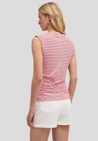 Top sin mangas a rayas rojas y blancas con detalles fruncidos en la parte posterior, combinado con pantalones cortos blancos. Material de algodón suave, corte clásico.