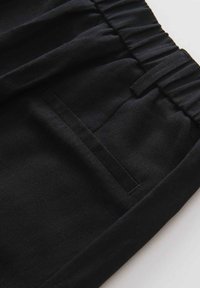 Pantaloni neri in lino con cintura elastica, dotati di una tasca laterale e una texture liscia. Progettati per comfort e facilità d'uso.