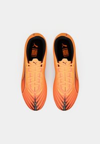 Oranžové sportovní boty s texturovaným povrchem, vybavené aerodynamickým tvarem, černými akcenty a centrálním systémem tkaniček. Viditelné logo PUMA.