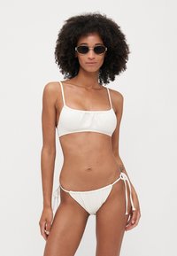 Hvit bikini sett med teksturert crop-top med justerbare stropper og lavt midjebelte med knyting i sidene. Glatt stofffinish.