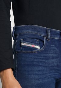 Mörkblå denimjeans med slim fit, med kontrastsömmar och en logotagg på bakfickan. Materialet verkar slätt och hållbart.