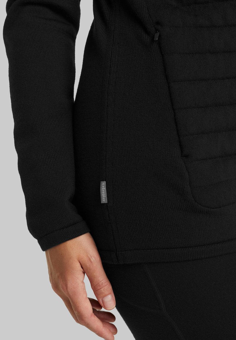 Schwarzer Pullover mit geripptem Strickmuster, ausgestattet mit einem quilted Paneel und einer seitlichen Tasche. Logostick auf dem Saum. Figurbetonter Schnitt mit langen Ärmeln.