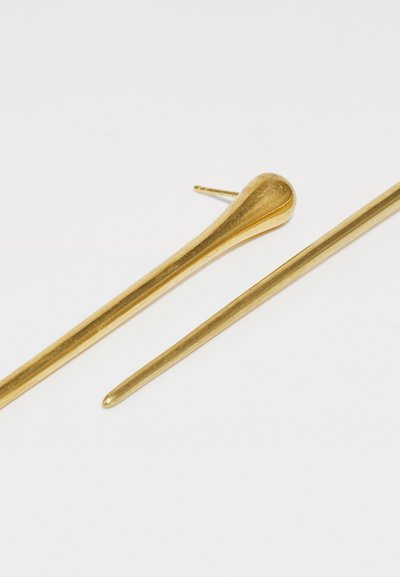 Alfileres de metal dorado, uno con punta redondeada y otro con punta afilada, sobre un fondo blanco. Textura suave, diseño elegante.