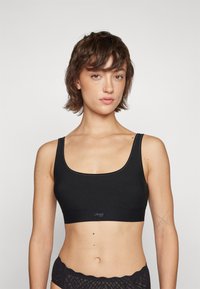 Soutien-gorge de sport noir avec un décolleté en U et des bretelles larges. Fabriqué en tissu lisse avec un logo sur la bande. Design simple et sans coutures.