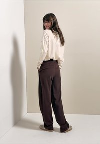 Pull à manches longues crème à coupe décontractée, associé à un pantalon large marron foncé. Tissu doux, design minimaliste et contraste de couleurs douces.