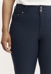 Marineblaue Denim-Hosen mit glatter Oberfläche, die ein klassisches Fünf-Taschen-Design und einen doppelten Knopfverschluss am Bund aufweisen.