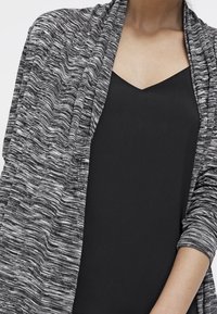 Femme portant un haut sans manches noir sous un cardigan ouvert gris et blanc chiné, vu du cou au milieu du bras.