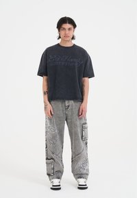 Mørkegrå oversized t-shirt med "Ed Hardy 1971" print, parret med løst siddende grå cargo bukser med hvide mønstre.