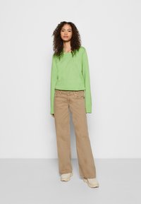 Suéter de malha verde claro com mangas longas, combinado com calças largas bege e ténis bege. Design de roupa simples e casual.