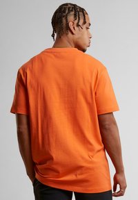 Oransje bomulls t-skjorte med korte ermer, løs passform og rund hals. Synlig søm detaljer bak og glatt tekstur.
