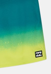 Costumi da bagno con gradiente in verde teal e verde lime, caratterizzati da una texture liscia, orlo arrotondato e un patch logo cucito nell'angolo in basso a destra.