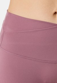 Højtaljede leggings i et blødt mauve materiale, med en glat tekstur, diskrete syninger og et tætsiddende design for komfort.