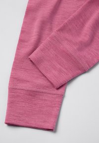 Close-up van een roze lange mouw stof met gebreide manchet en gedetailleerd stikwerk op een lichtgrijze achtergrond.