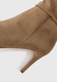 Stivaletto in suede marrone con tacco alto affusolato, caratterizzato da una texture liscia e da cuciture minime, che mette in evidenza un design elegante e slanciato.