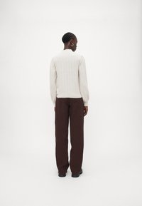 Maglione di colore crema chiaro, a costine e con maniche a palloncino, abbinato a pantaloni larghi di colore marrone scuro. Texture morbida, design semplice e cuciture discrete.