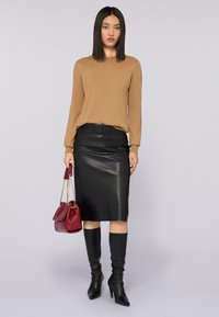 Maglione marrone a maniche lunghe, gonna a tubino in pelle nera aderente, stivali neri fino al ginocchio, tiene una borsa bordo con tracolla a catena.