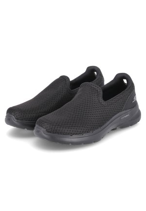Zapatos negros tipo slip-on hechos de tela de malla que cuentan con una superficie texturizada, una suela acolchada y un diseño de punta redondeada, ofreciendo un ajuste ligero.
