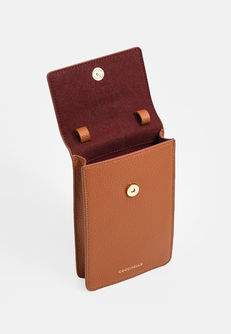 Skórzana torba na ramię w kolorze brązowym z złotym zapięciem na zatrzask i burgundowym zamszowym wnętrzem, z logo "Coccinelle" z przodu.