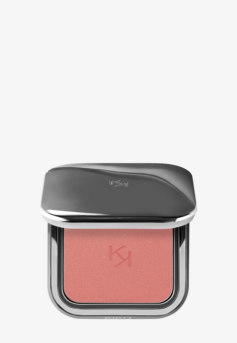 Poederroze blush in een zachte rozentint, verpakt in een vierkante zilveren compact met een gebogen deksel en een gegraveerd logo. Zachte, matte textuur zichtbaar.