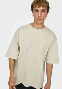 Beige oversized t-shirt lavet af blødt stof, med rund halsudskæring og brede ærmer; glat tekstur med en afslappet, løs pasform.