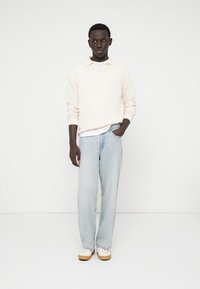 Cremefarvet ribstrikket sweater, lyseblå vide jeans og beige sko. Simpelt design med blød tekstur og afslappet pasform.