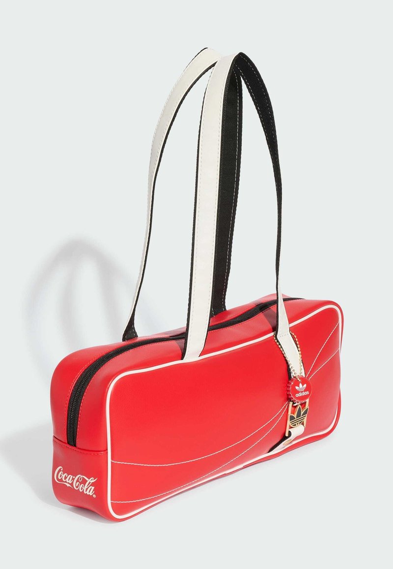 Red rectangular shoulder bag with white trim, black and white straps, Coca-Cola logo on side, and Adidas bottle cap keychain attached.