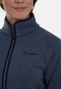 Fleecejack in donkerblauw met een hoge kraag en volledige rits. Kenmerkt zich door tonale stiksels en een subtiele logo op de linkerborst. Zachte textuur.