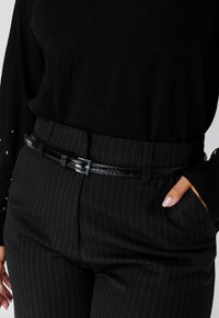 Zwart gestreepte broek heeft een gladde textuur,accentueert door een glanzende zwarte riem met een rechthoekige zilveren gesp. Een zwarte top maakt de look compleet.