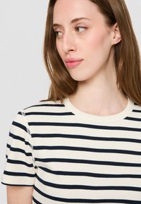 Rutet t-skjorte med marineblå og off-white horisontale striper. Rund hals, korte ermer og mykt bomullsmateriale med en jevn tekstur.