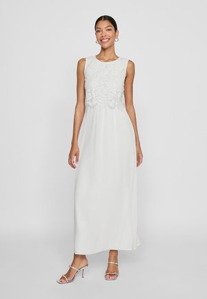 White maxi dress with a lace bodice and sleeveless design, flowing skirt, and smooth texture. Paired with silver strappy heels.