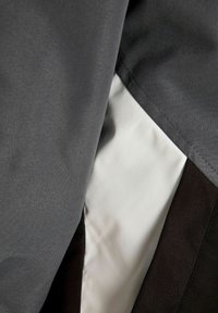 Κοντινό πλάνο διαστρωματωμένων γκρι, λευκών και σκούρων καφέ υφασμάτινων πάνελ με ορατή ραφή και ομαλή υφή.