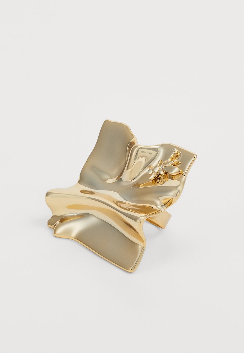 Gold-toned ring holder with a wavy, organic shape. Features a floral accent with small stones and a smooth, glossy finish.