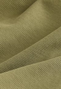 Gros plan sur un tissu vert olive texturé avec un petit motif tricoté tissé et des plis doux créant des ombres.