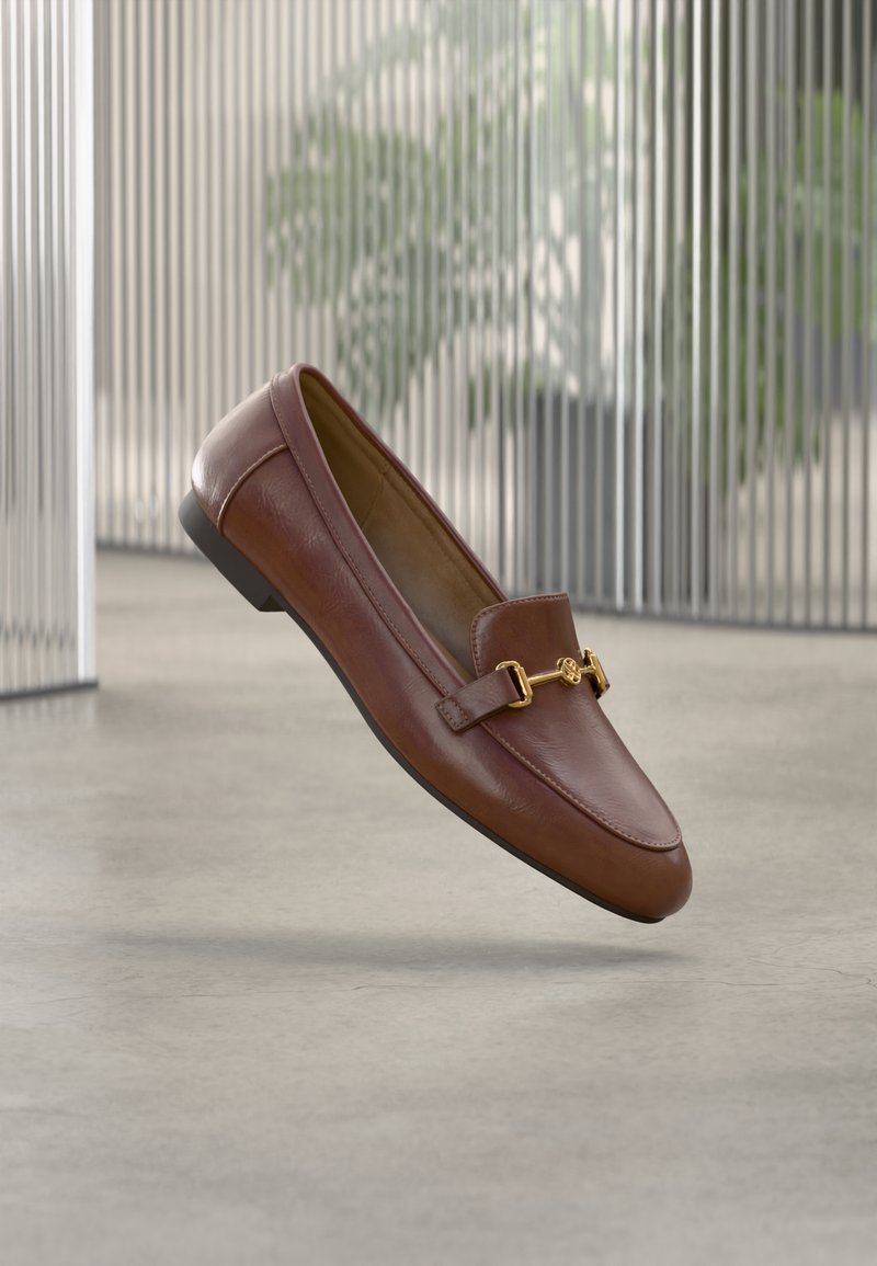Mocassins en cuir marron avec un bout arrondi, des accents en métal doré et une semelle plate. Ils présentent un design épuré et une texture lisse.