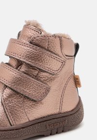 Dětská kožená bota v barvě růžového zlata se dvěma suchými zipy, texturovanou podrážkou a chlupatým podšívkou viditelnou na horním okraji.