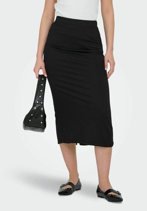Zwarte midi-rok van rekbaar materiaal, met een hoge tailleband. Vergezeld van een zwarte handtas met zilveren studs en platte schoenen.