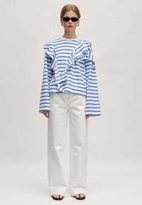 Gestreepte lange mouwen top met gerimpelde details in blauw en wit; gecombineerd met witte wijde broek en zwarte slippers. Inclusief accessoires.