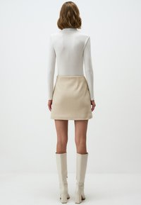 Weißes Langarmoberteil mit geripptem Design, kombiniert mit einem beigen A-Linien-Rock. Modell trägt weiße knielange Stiefel; minimalistisches Design.