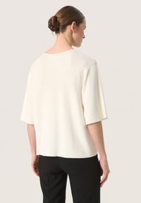 Cream-colored sweater with short sleeves, a relaxed fit, and a round neckline. Soft fabric with a smooth texture and a straight hem.