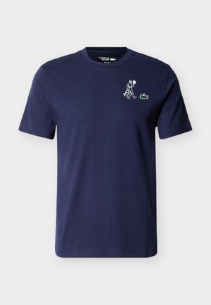 Tricou bleumarin cu mânecă scurtă, cu un mic desen alb cu un jucător de tenis și logo-ul crocodilului Lacoste verde pe partea stângă a pieptului.