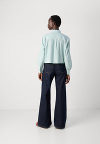 Mintgrönrandig blus med långa ballongärmar, kombinerad med utsvängda mörkblå jeans. Blusen har en knapppdetailj vid ärmslut och en rundad nederkant.