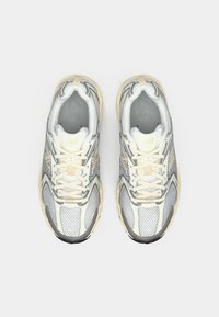 Witte en grijze hardloopschoenen van New Balance met beige accenten, gezien van bovenop op een effen witte achtergrond.