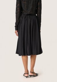 Gonna nera plissettata realizzata in tessuto leggero. Presenta una vita elastica e una leggera lucentezza con lunghezza a metà polpaccio. Design semplice e fluido.