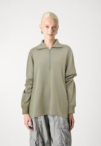 Lys grønn, langermet quarter-zip genser i myk stoff med høy krage og rund glidelås, kombinert med grå cargo bukser.
