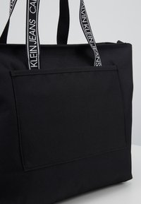 Czarna torba na ramię z przednią kieszenią i markowymi czarno-białymi paskami na ramię Calvin Klein Jeans.